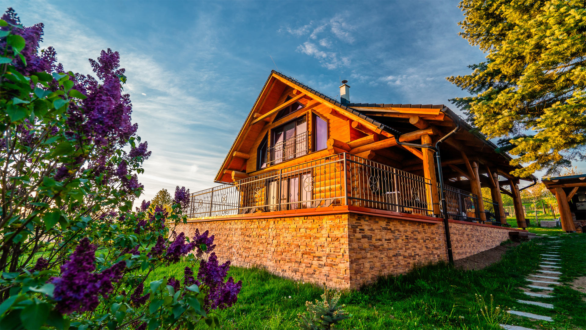 Zrub Živa – pohľad na drevenicu s terasou pri lese, v pozadí rozhľadňa Vartovka pri Krupine